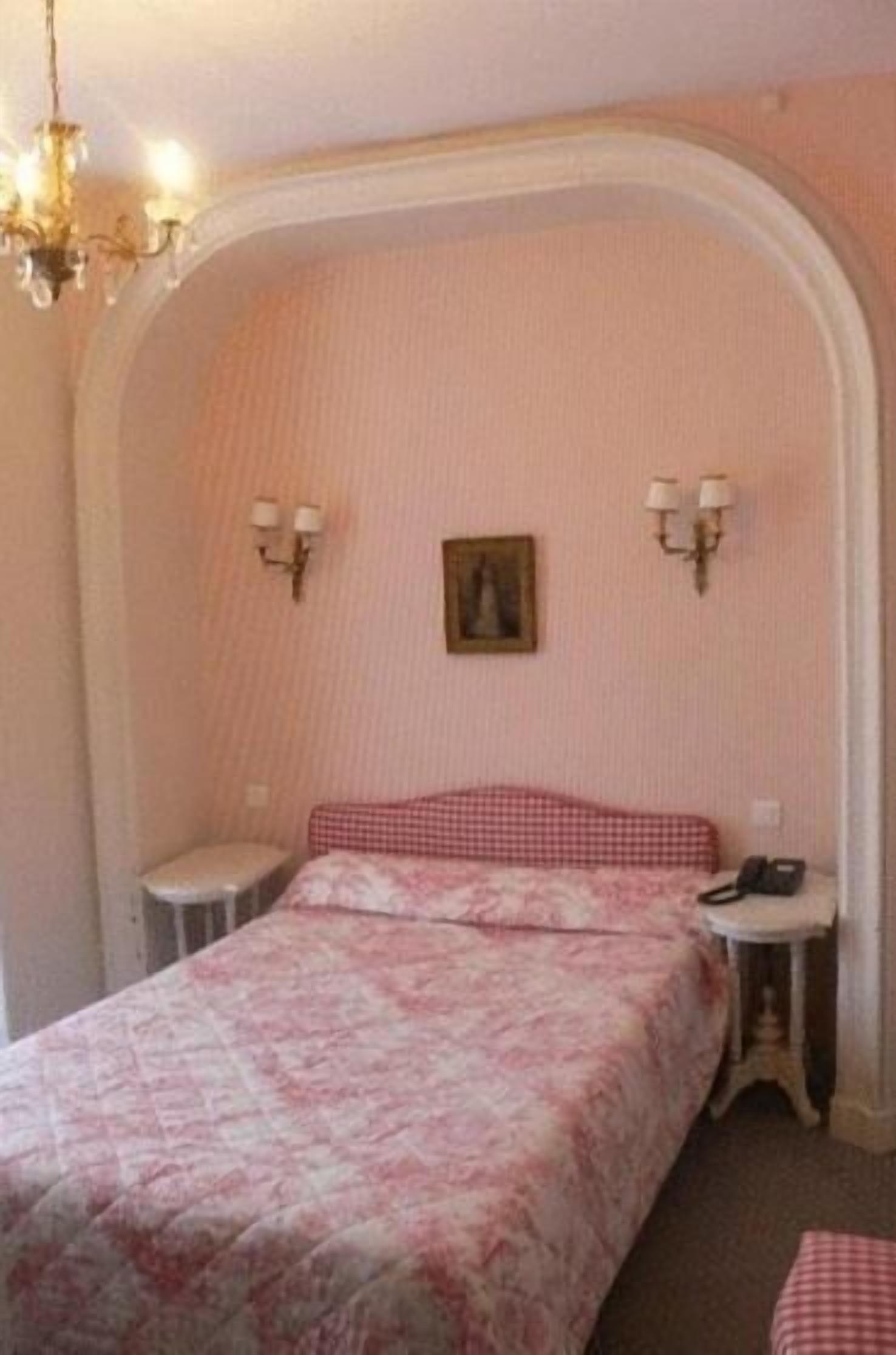 Une chambre à coucher avec un lit double, une petite table de chevet, une chaise, un tableau accroché au mur et un lustre.