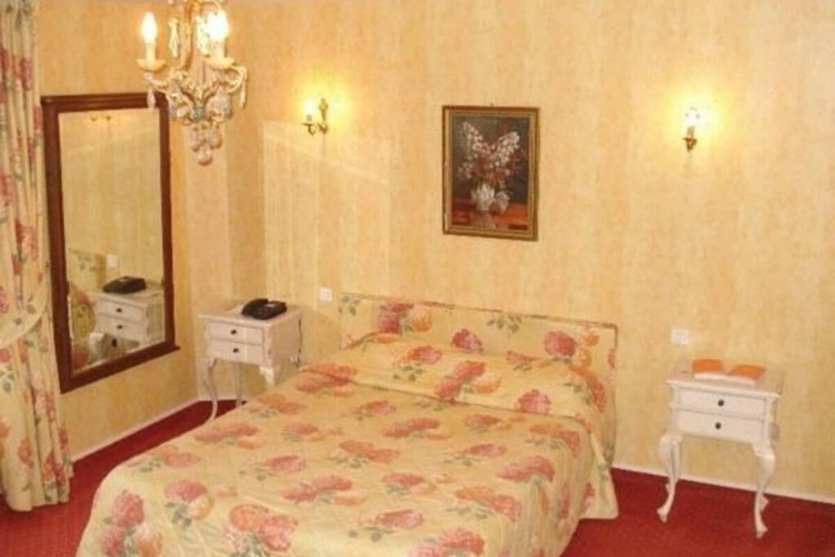Een slaapkamer met een groot bed, een spiegel, nachtkastjes en een kroonluchter.