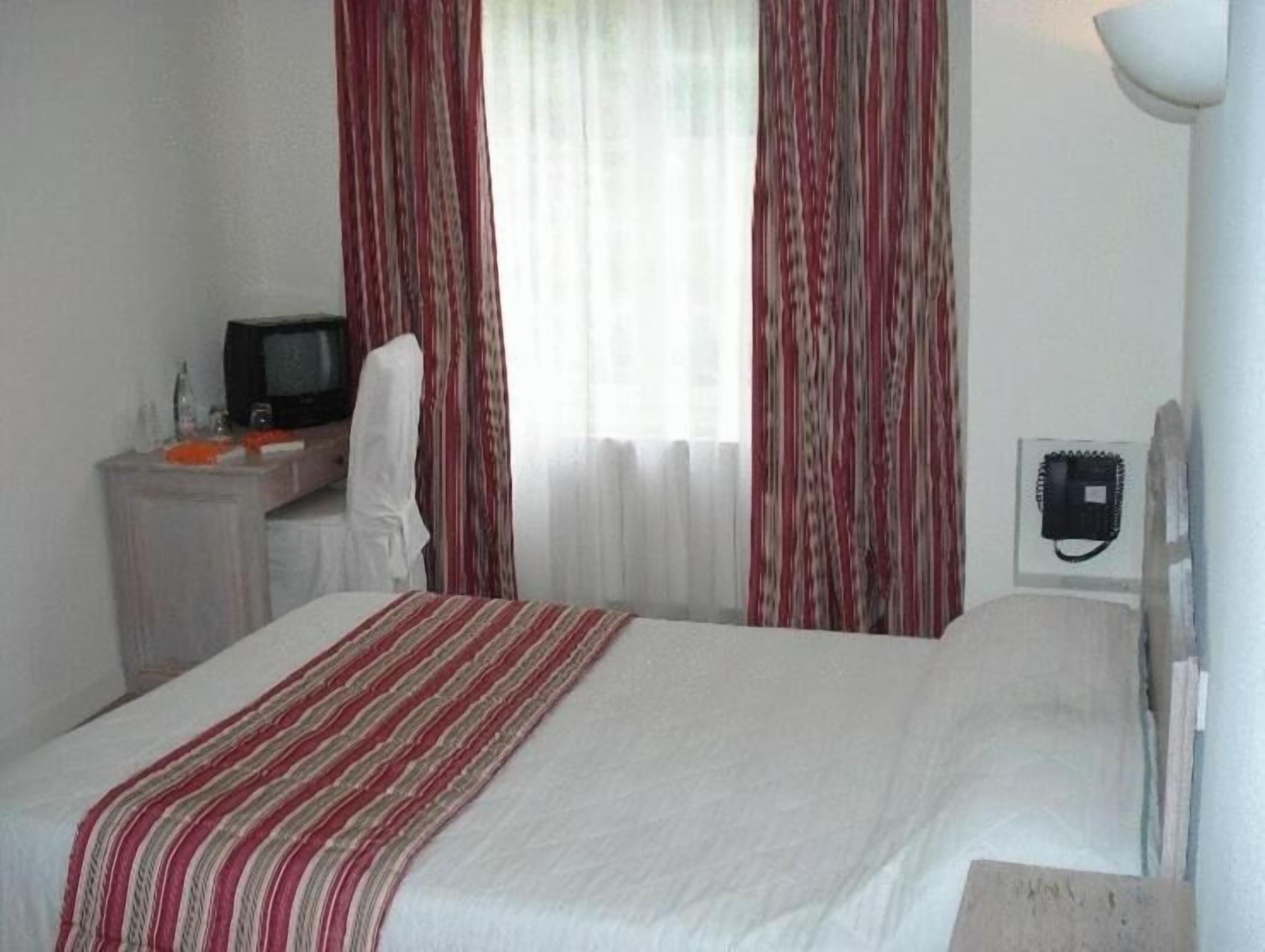 Una habitación de hotel con una cama, un escritorio con televisor y un teléfono.