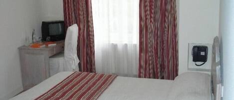 Una habitación de hotel con una cama, un escritorio con televisor y un teléfono.
