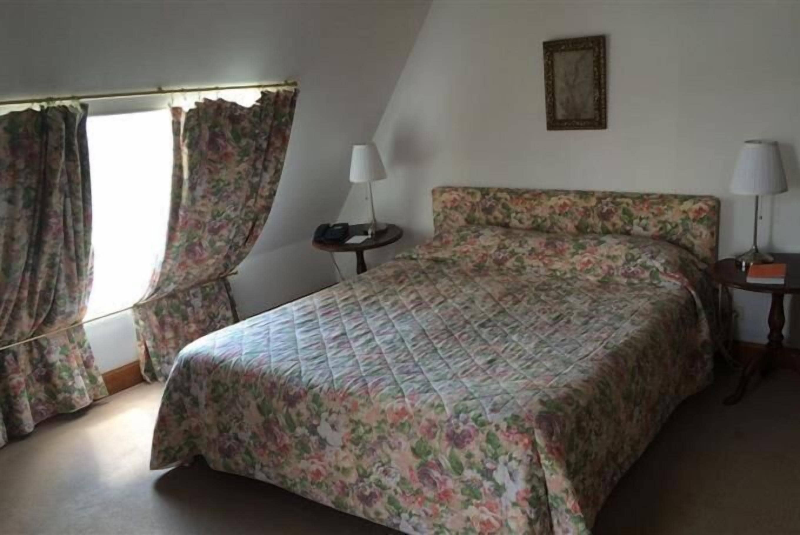 A bedroom with a bed, a nightstand, a lamp, and curtains.