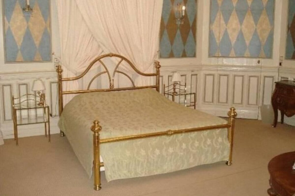 Een slaapkamer met een hemelbed, nachtkastje en stoel.