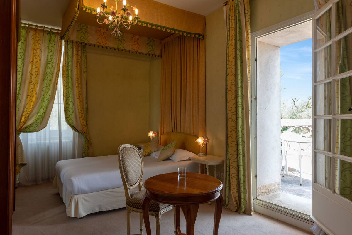 A bedroom with a bed, a chair, a small table, and a window with curtains.