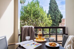 Un balcón con una mesa dispuesta para el desayuno, que incluye una botella, vasos, una taza y bollería.