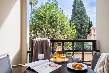 A balcony with a table set for breakfast, including a bottle, glasses, a cup, and pastries.