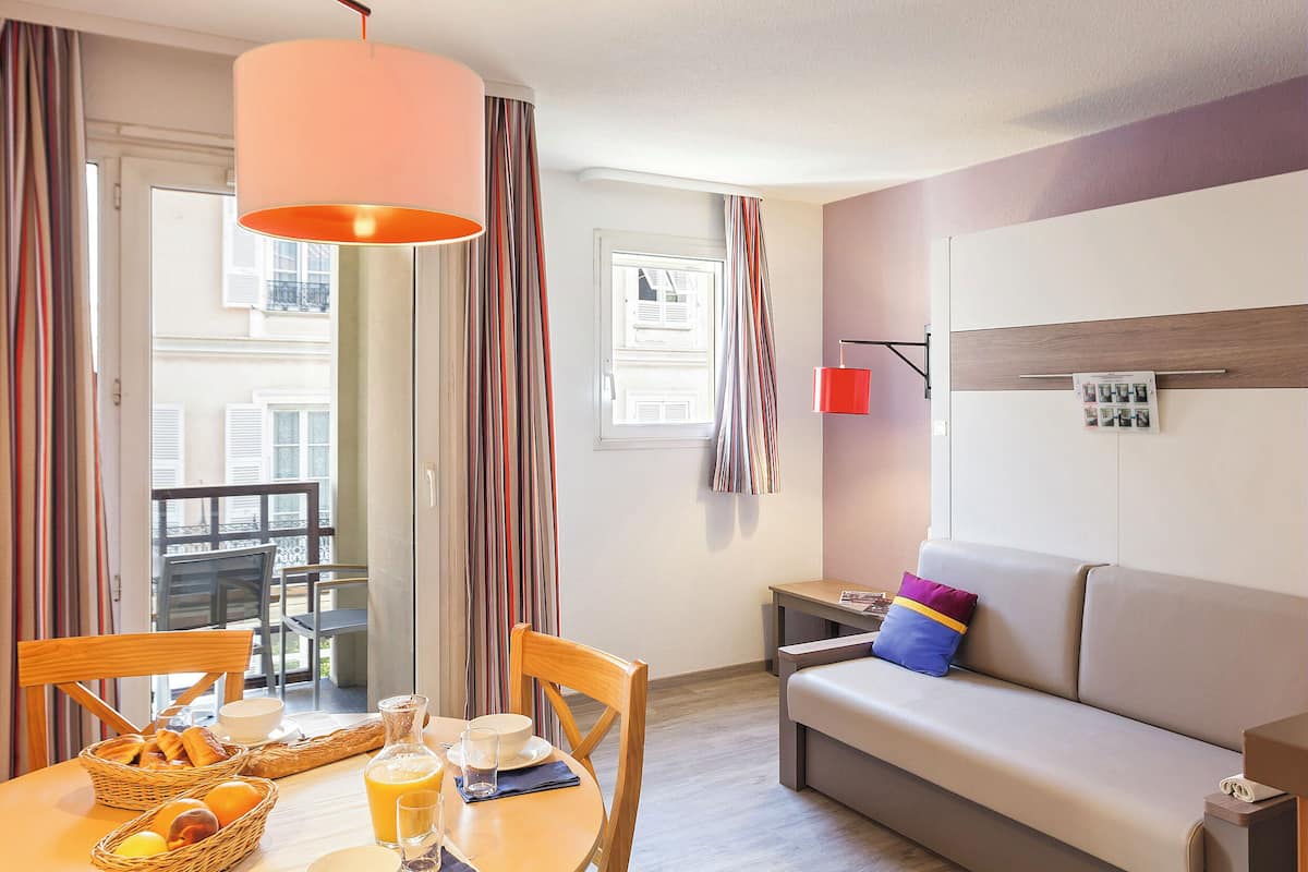Een moderne hotelkamer met een ontbijt gedekte eettafel, een bank en uitzicht op de stad.