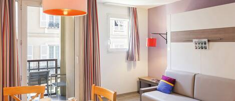 A modern hotel room with a dining table set for breakfast, a sofa, and a view of the city.