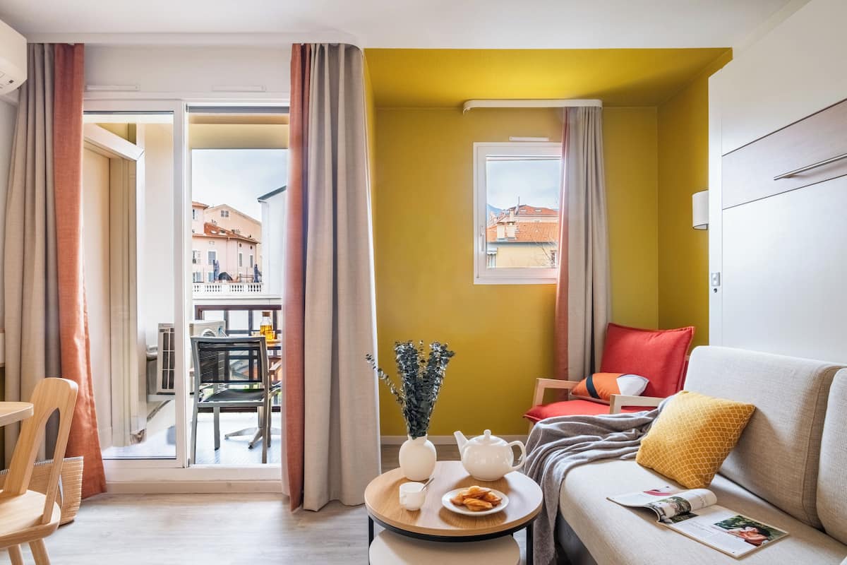 Een moderne woonkamer met een bank, een kleintje tafeltje met een theepot en gebak, en uitzicht op het balkon.