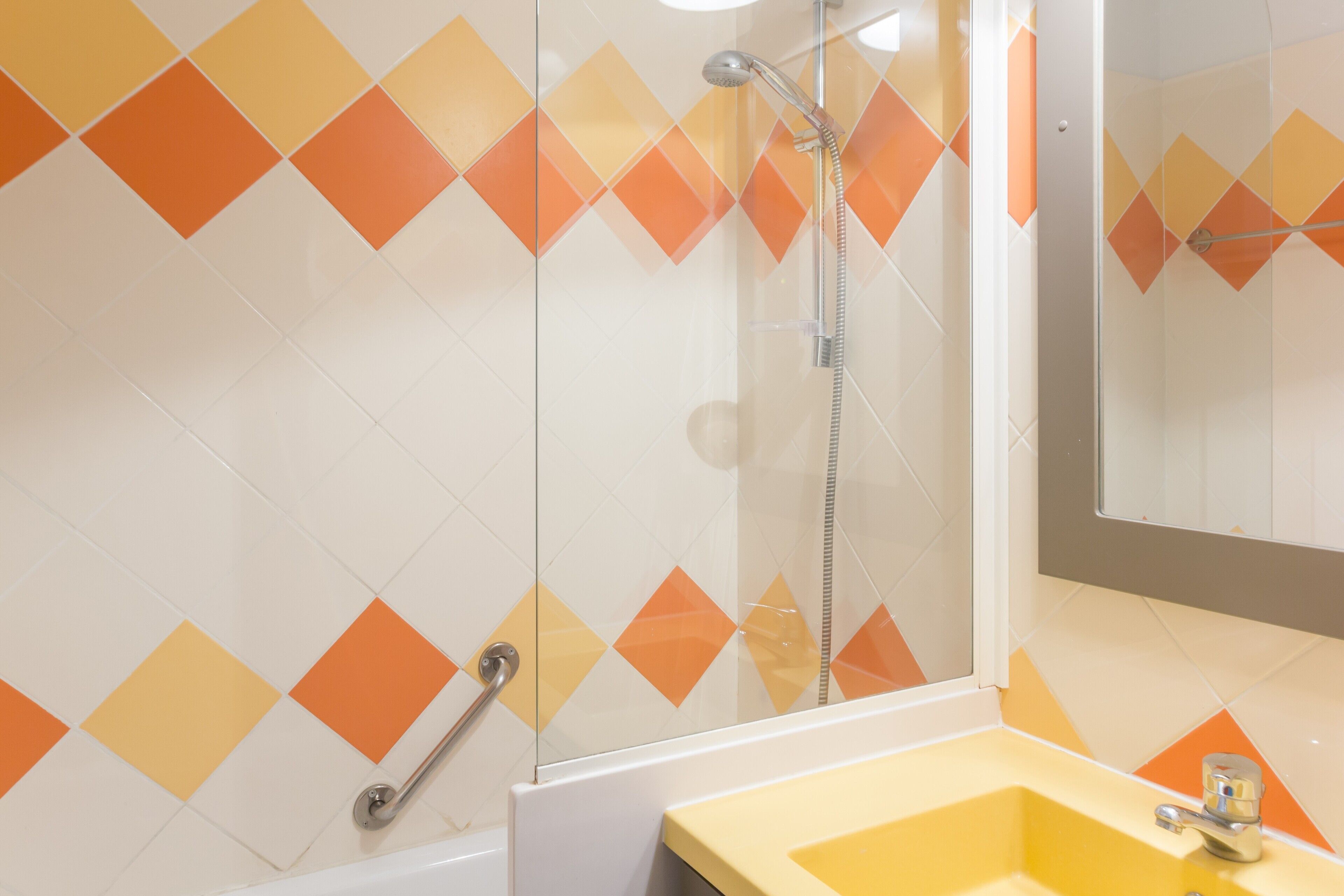 A bathroom with a yellow sink, a glass shower enclosure, and a wall with a diamond pattern of orange and white tiles.