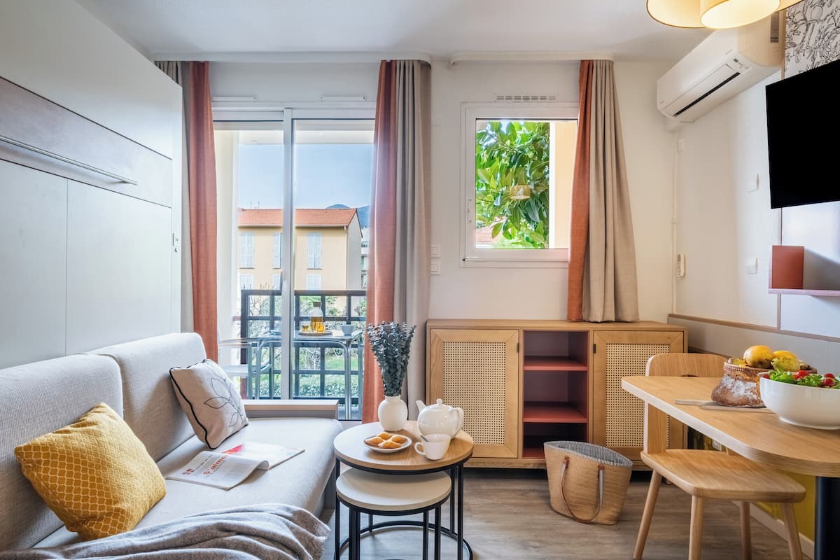 Een moderne woonkamer met een bank, een klein rond tafeltje, een eettafel en uitzicht naar buiten.
