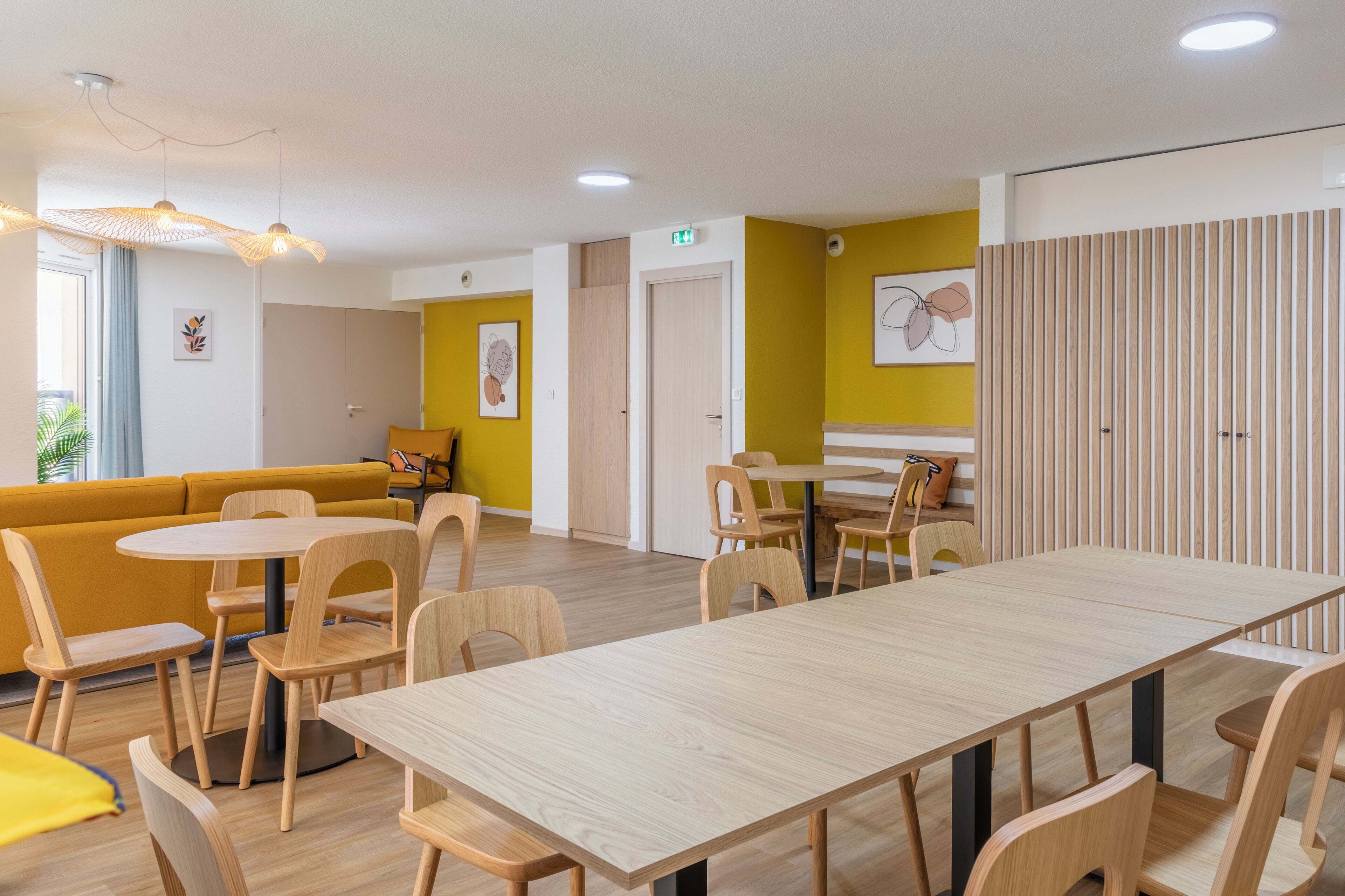 Et moderne interiør med et langt spisebord, flere stole, en gul sofa og en skillevæg i træ.