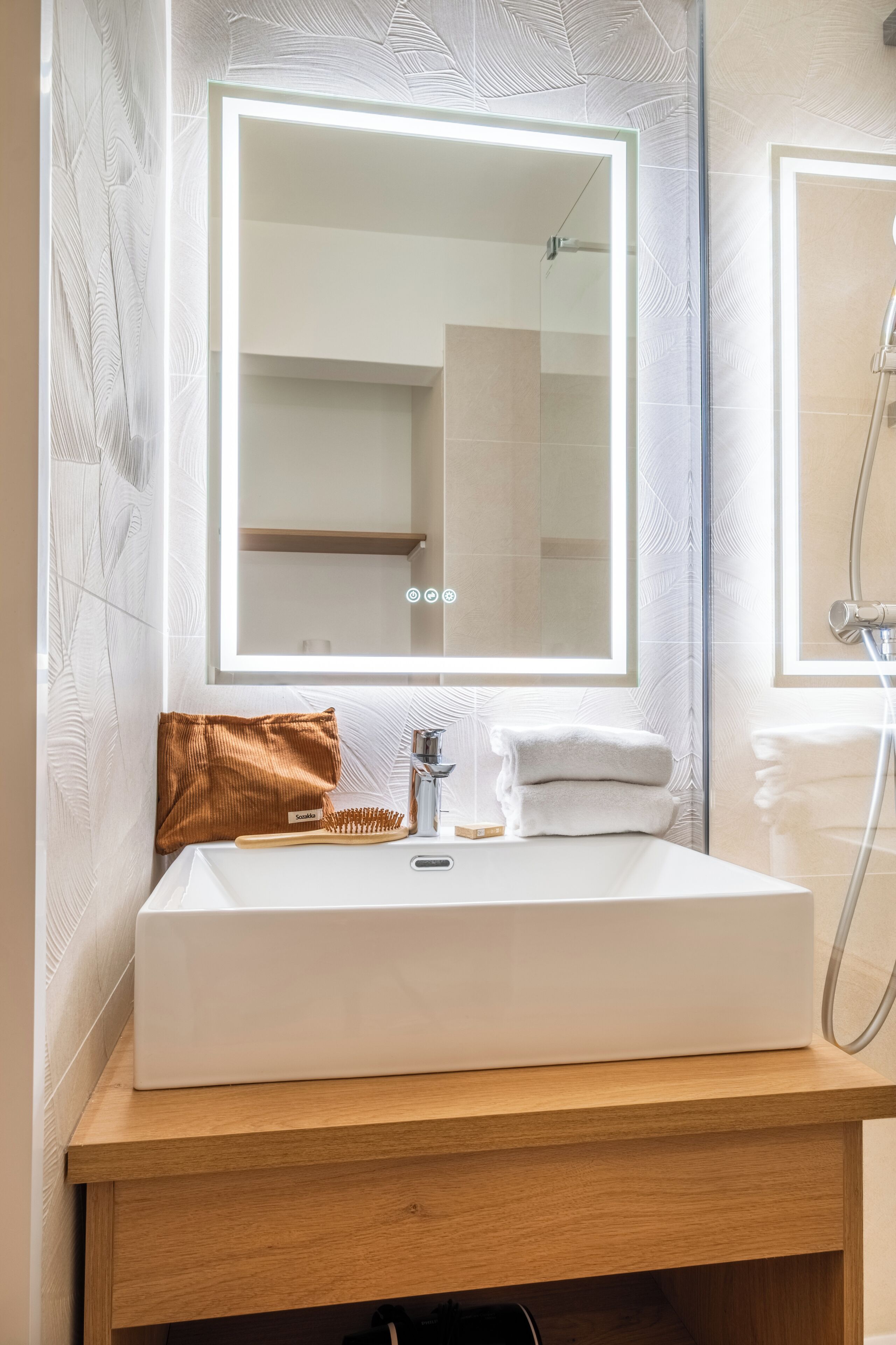 A bathroom with a white sink, a mirror, a towel, and a shower.