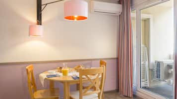 A dining area with a table set for two, a wall-mounted air conditioner, and a window with curtains.