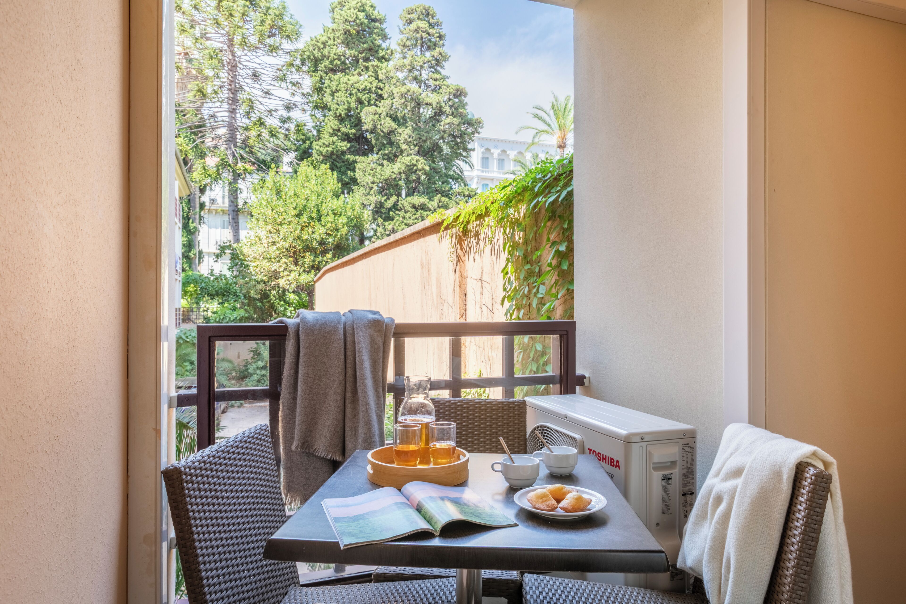 A balcony with a table set for breakfast, including a book, a plate of croissants, and a glass of beer.
