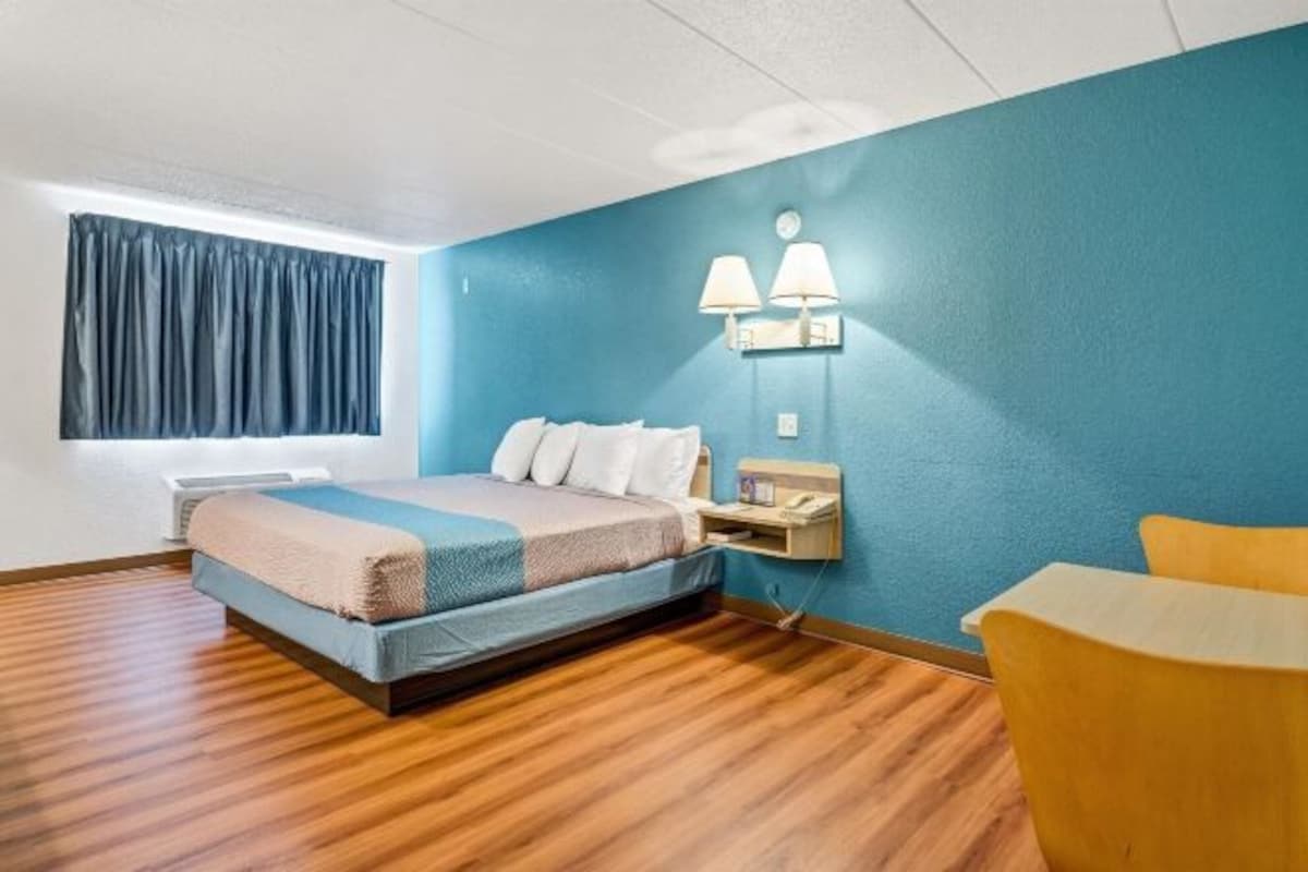 A hotel room with a bed, bedside table, lamp, and a window with curtains.