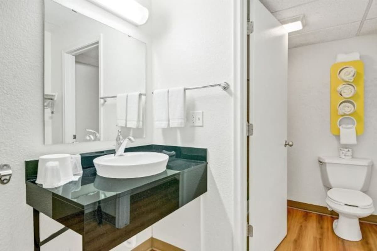 A modern bathroom with a glass sink, white fixtures, and a yellow towel dispenser.
