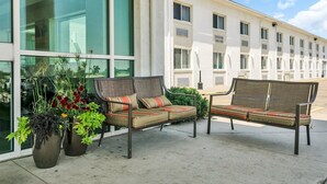 Een terras met twee stoelen en een tafel, plantenpotten en een gebouw met grote ramen op de achtergrond.