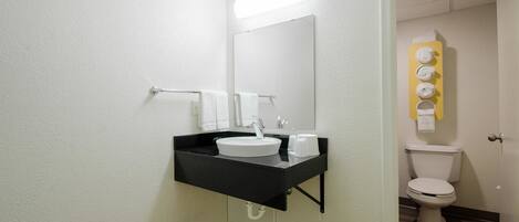 A bathroom with a white sink, black countertop, and a mirror above it. There is a towel rack with white towels and a toilet visible in the background.