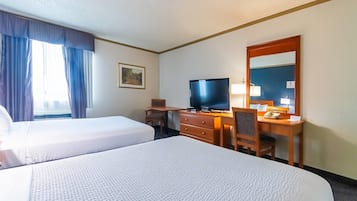 Habitación de hotel con dos camas, un escritorio con televisor, un espejo y una ventana con cortinas.
