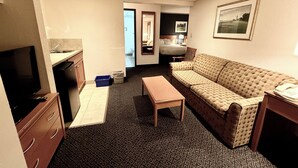A compact hotel room with a kitchenette, a sofa, a small table, and a TV.
