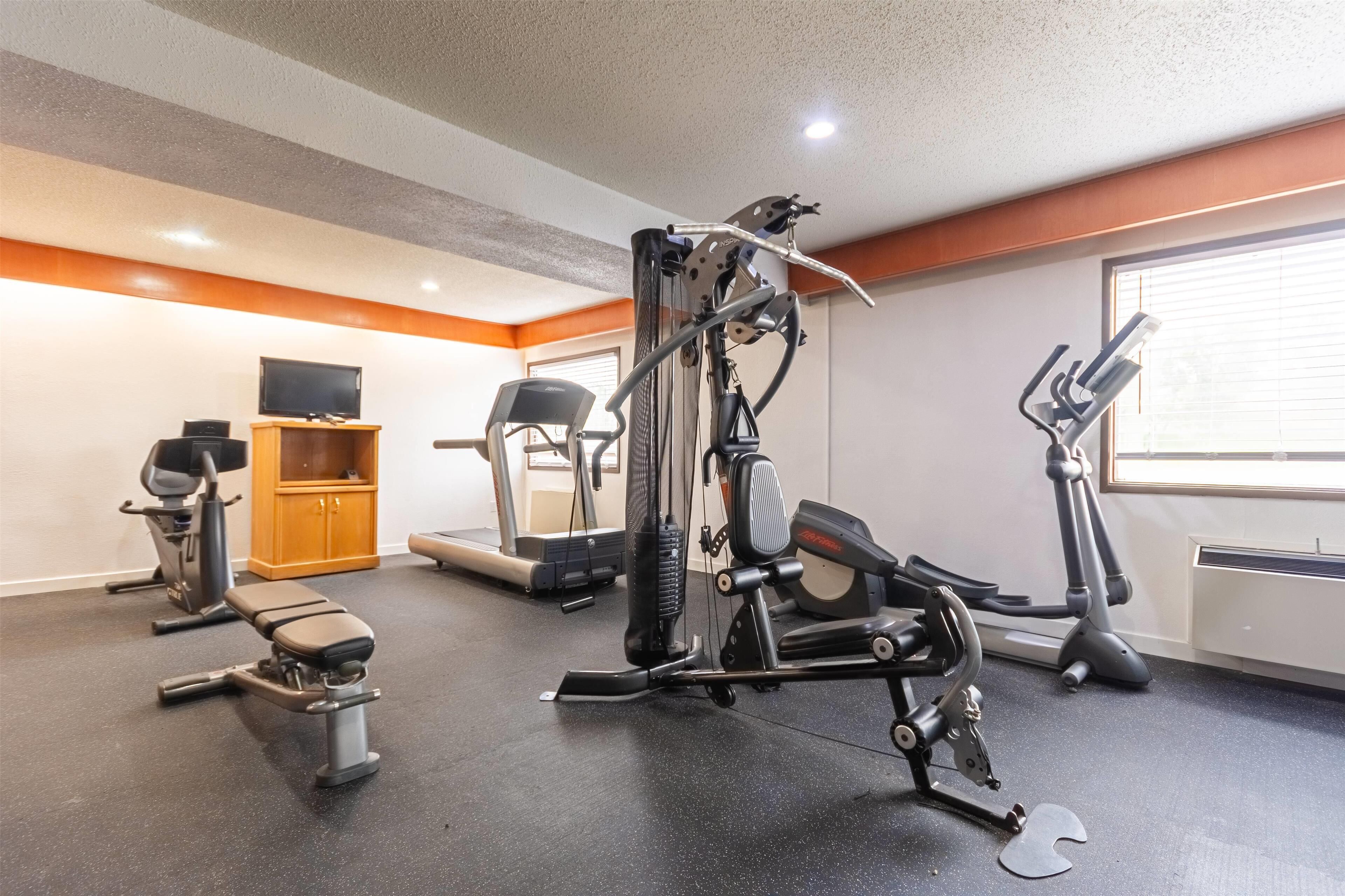 A gym with various exercise equipment, a television on a cabinet, and a window with blinds.
