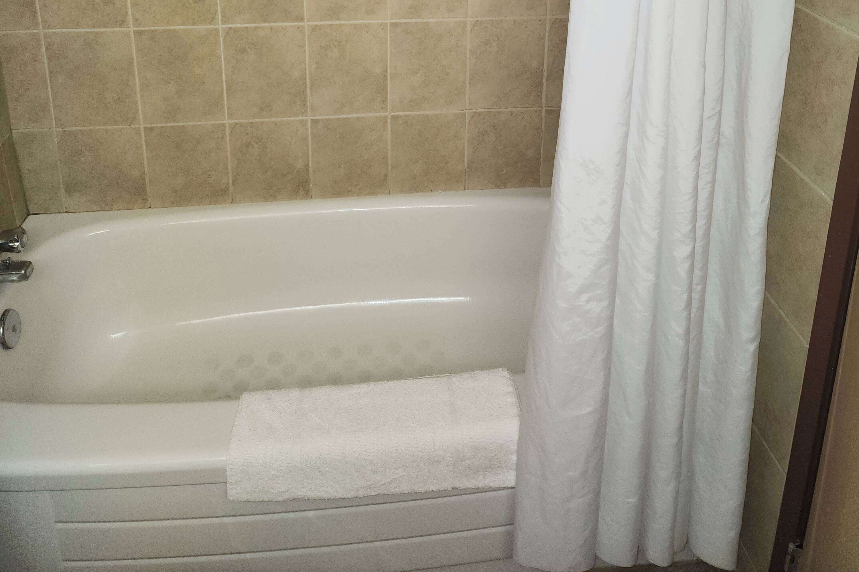 A bathtub with a white towel and a white shower curtain in a bathroom with beige tiled walls.