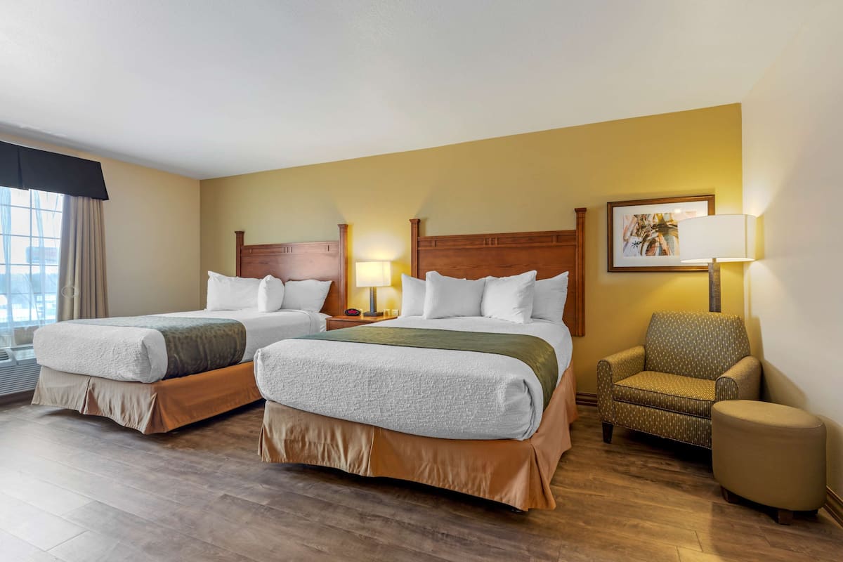 Ein Hotelzimmer mit zwei Betten, einem Sessel, einer Lampe und einem gerahmten Bild an der Wand.