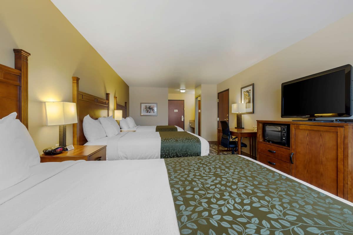 Ein Hotelzimmer mit zwei Betten, einem Fernseher, einem Schreibtisch mit Computer und einer Tür zu einem weiteren Raum.
