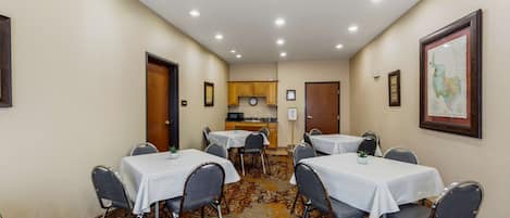 Un salón de conferencias con mesas y sillas, una zona de cocina y suelo alfombrado.
