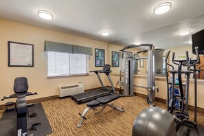 Uma academia com equipamentos de exercícios, esteira, aparelho de musculação e um quadro de segurança fixado na parede.