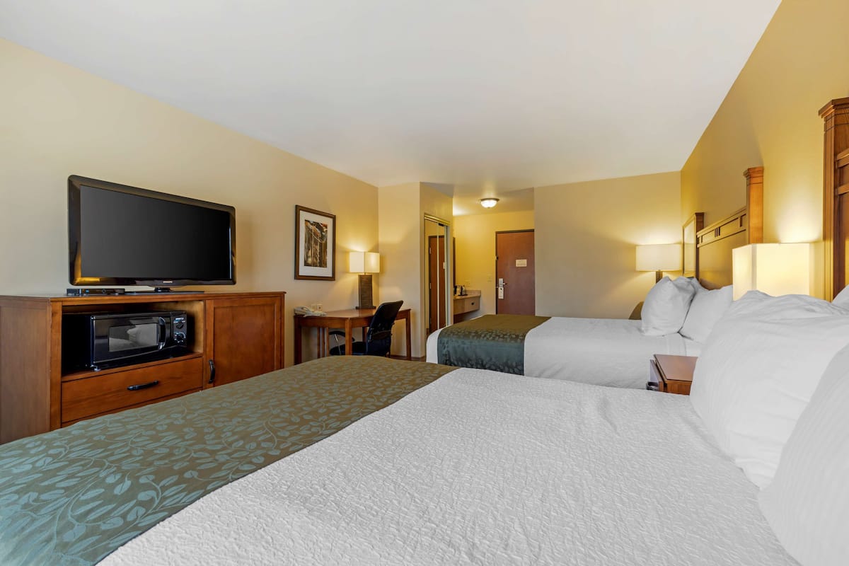 Ein Hotelzimmer mit einem großen Bett, einem Schreibtisch mit Stuhl, einer Mikrowelle, einem Fernseher und einer Tür zu einem weiteren Raum.