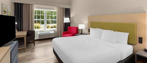 Habitación de hotel con una cama grande, un escritorio, una silla, un televisor y una ventana con cortinas.
