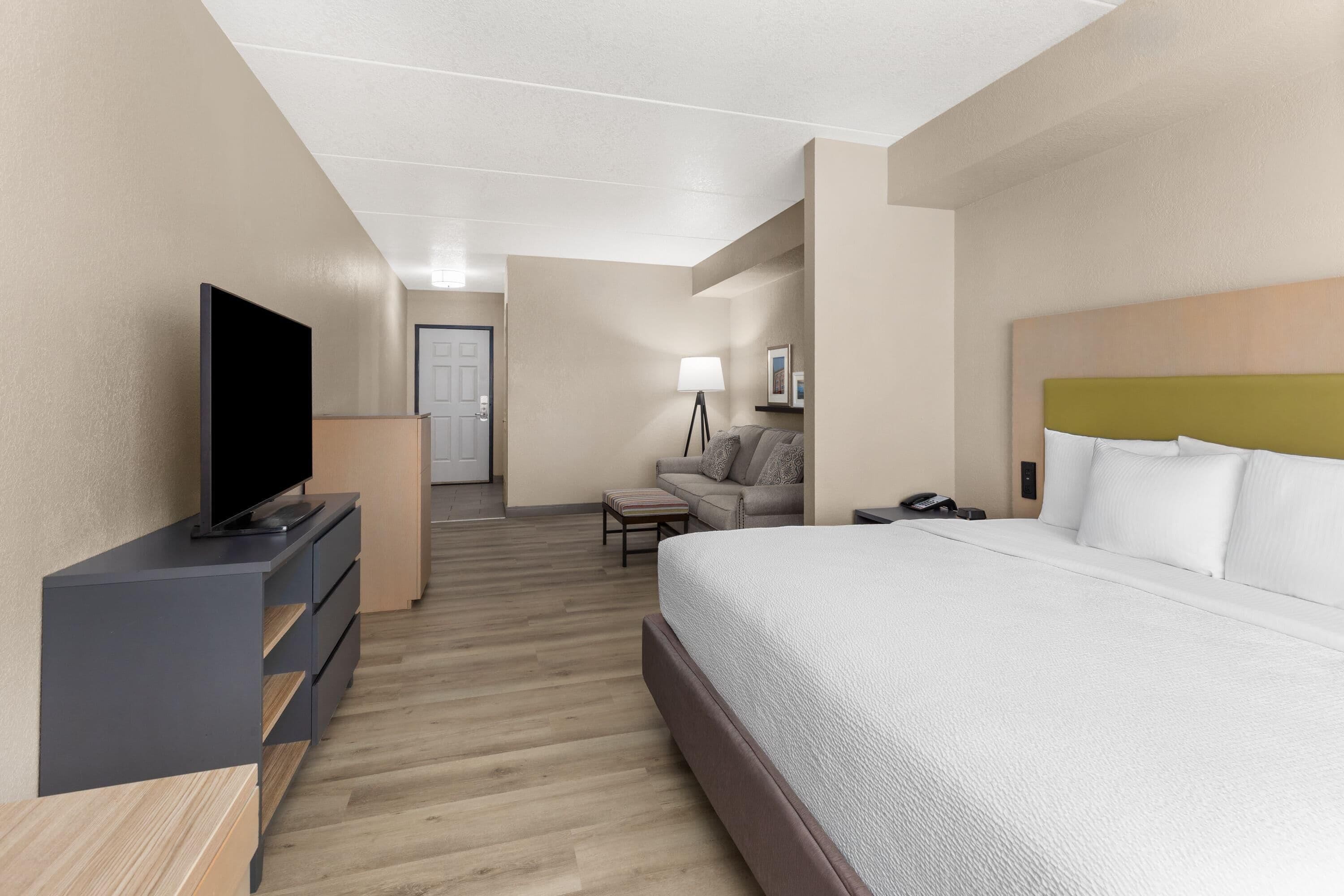 Una habitación de hotel con cama, televisión, escritorio, lámpara y sofá.