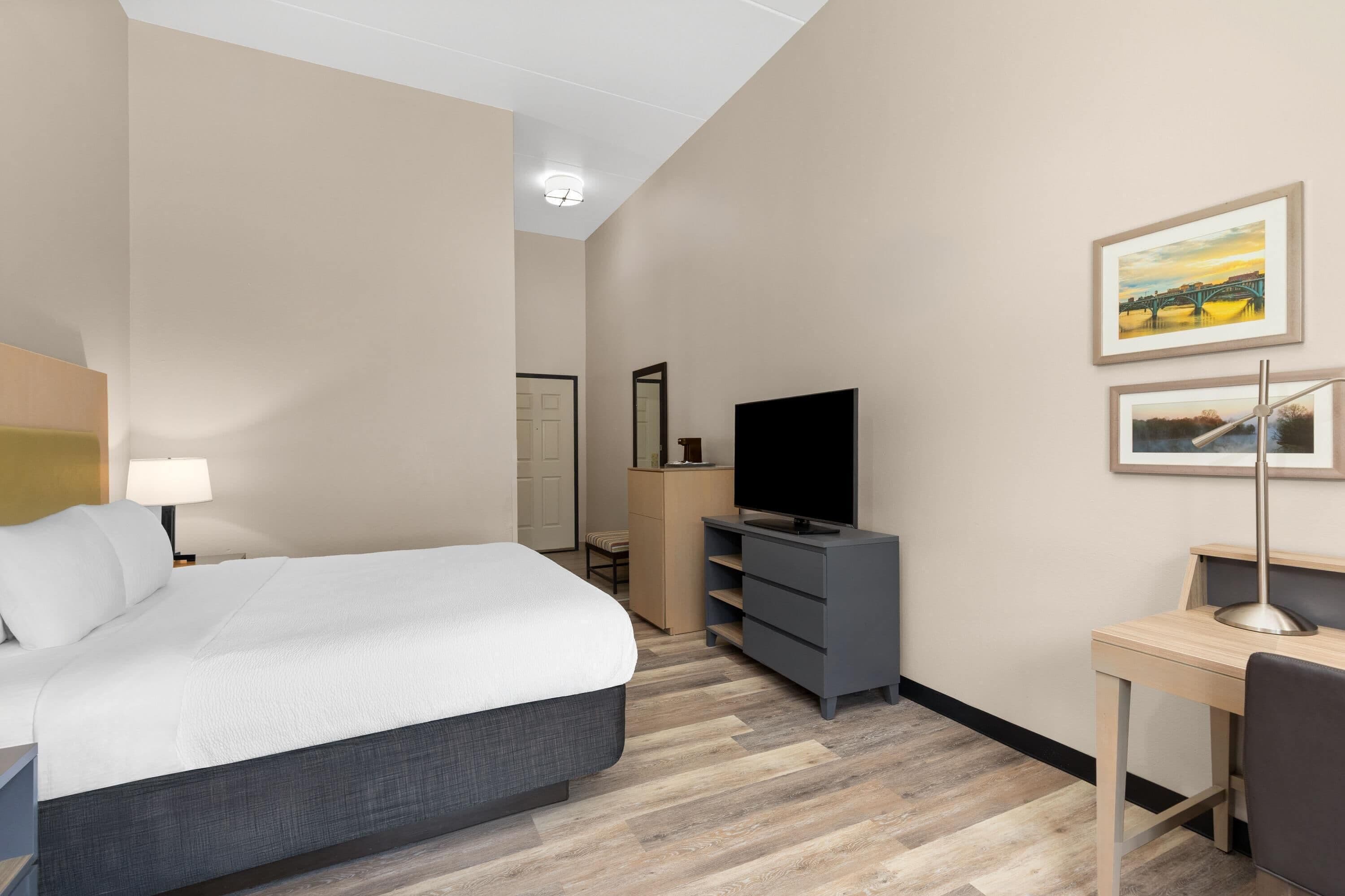 Una habitación de hotel con cama, escritorio, televisor y espejo.