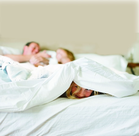 A bedroom with a bed covered by white sheets and a white blanket.