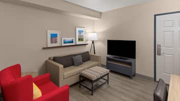 A hotel room with a sofa, a red armchair, a television, and a door.