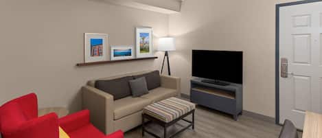 Une chambre d’hôtel avec un canapé, un fauteuil rouge, une télévision et une porte.