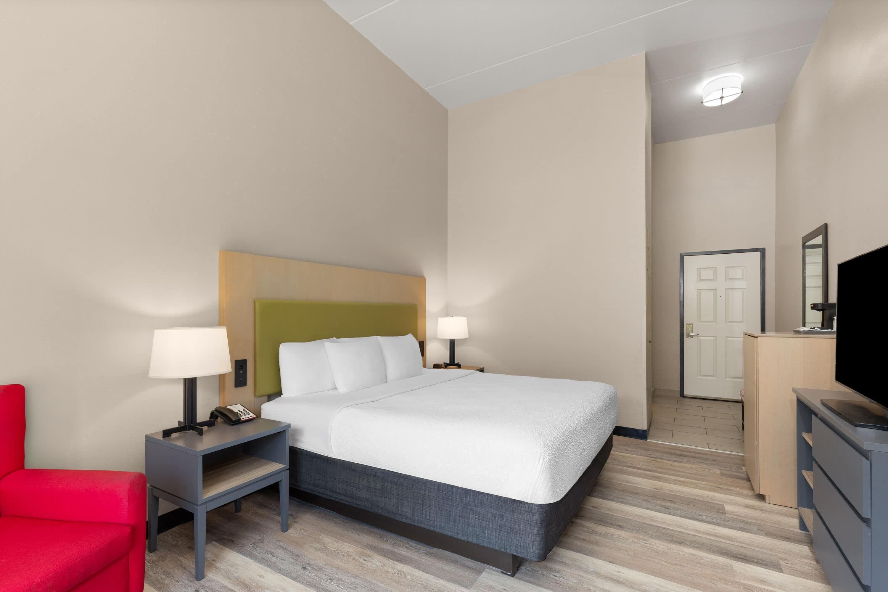 Ein Hotelzimmer mit Bett, Nachttischen, einem roten Sessel, einem Fernseher und einer Tür.
