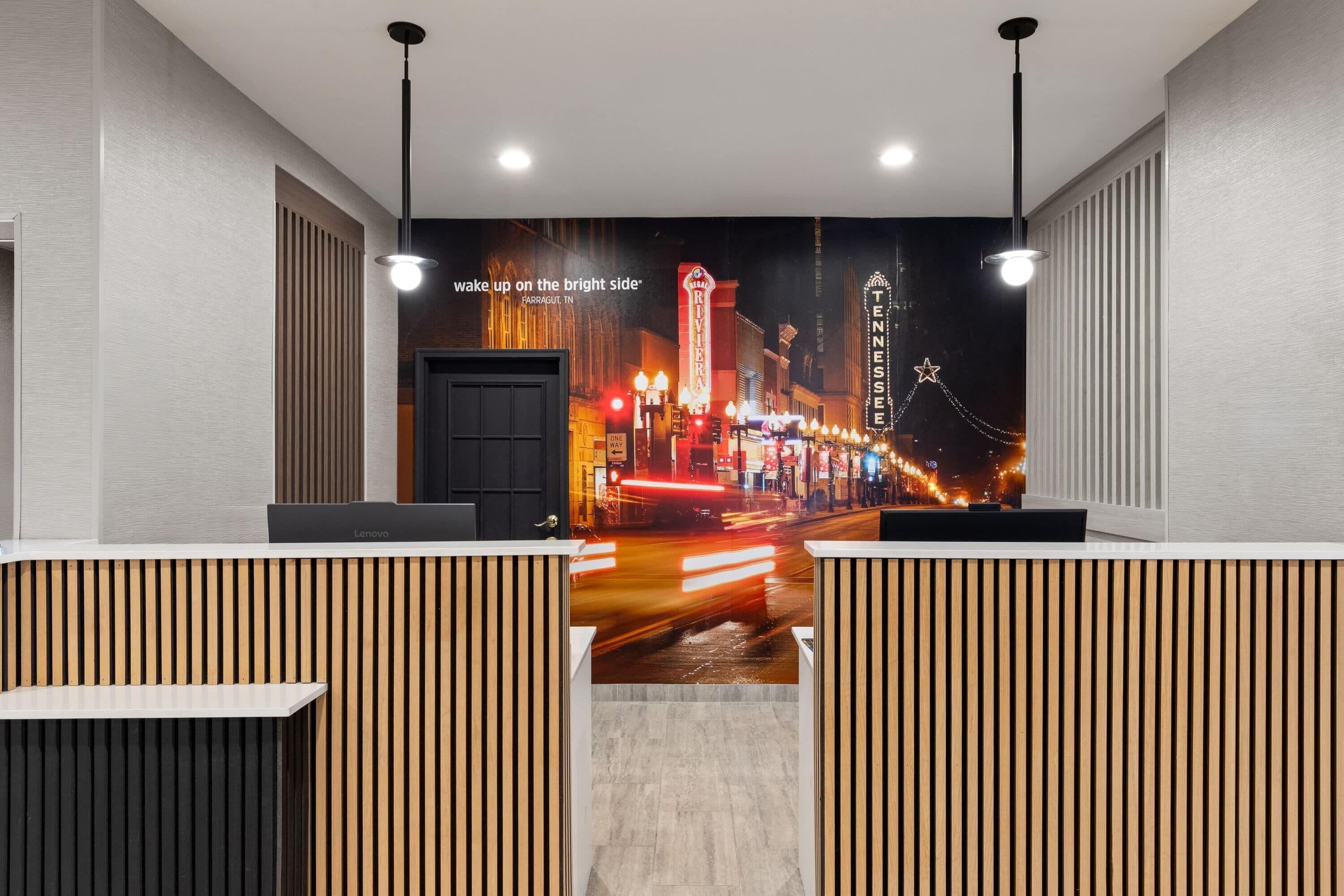 Un espace d’accueil d’hôtel agrémenté d’une fresque représentant un paysage urbain, de cloisons en panneaux de bois et d’un bureau Lenovo.