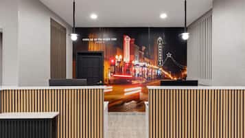 Un espace d’accueil d’hôtel agrémenté d’une fresque représentant un paysage urbain, de cloisons en panneaux de bois et d’un bureau Lenovo.