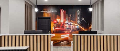 Zona de recepción de un hotel con un mural de la ciudad, separadores de madera y un escritorio Lenovo.