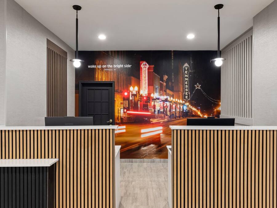 Un espace d’accueil d’hôtel agrémenté d’une fresque représentant un paysage urbain, de cloisons en panneaux de bois et d’un bureau Lenovo.
