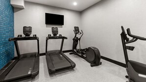 A fitness room with three treadmills, an elliptical, and a TV mounted on the wall.
