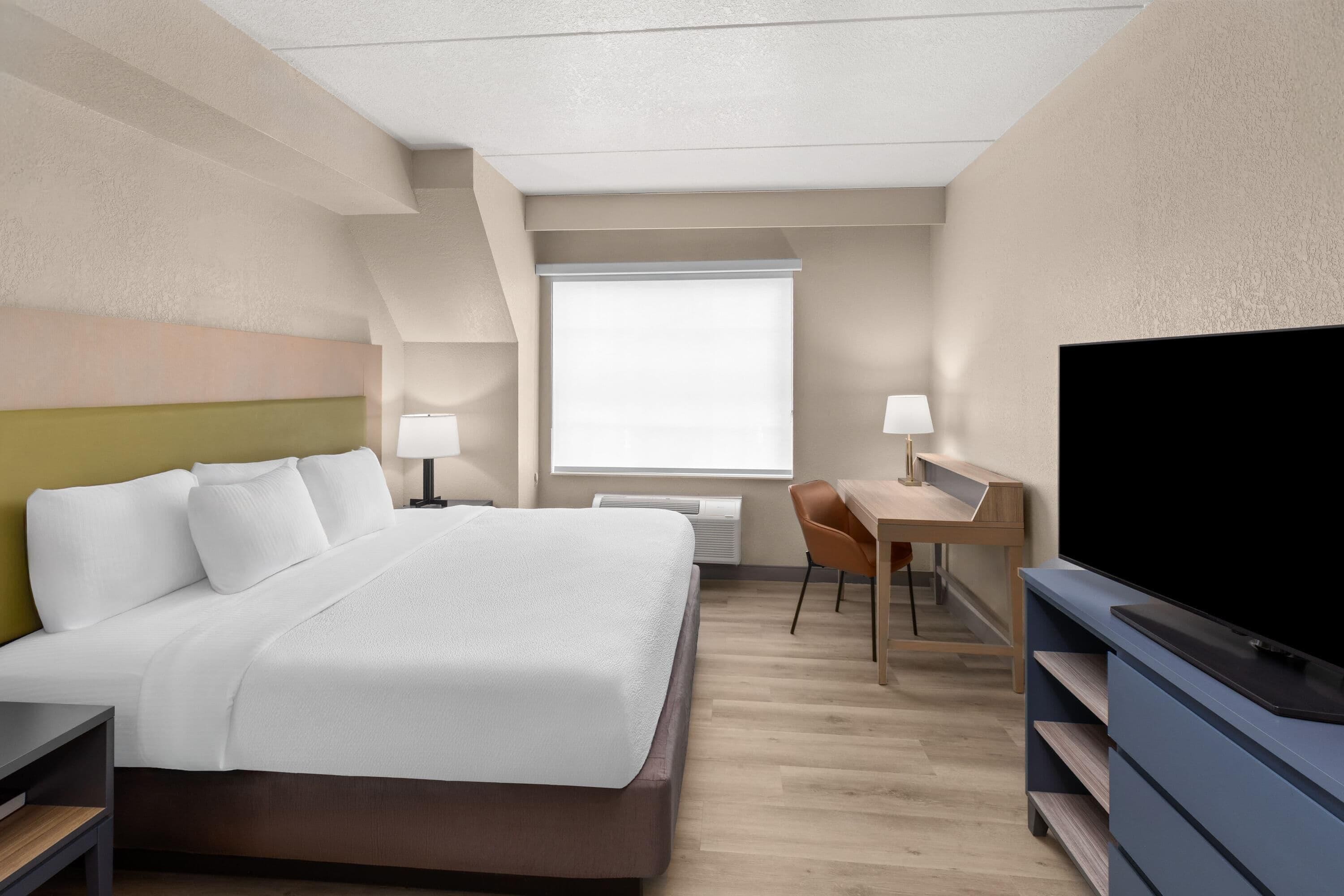 A hotel room with a bed, desk, chair, television, and a window.