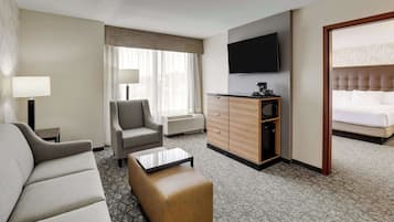 Habitación de hotel con sofá, sillón, reposapiés, televisor de pantalla plana, cama y minibar.