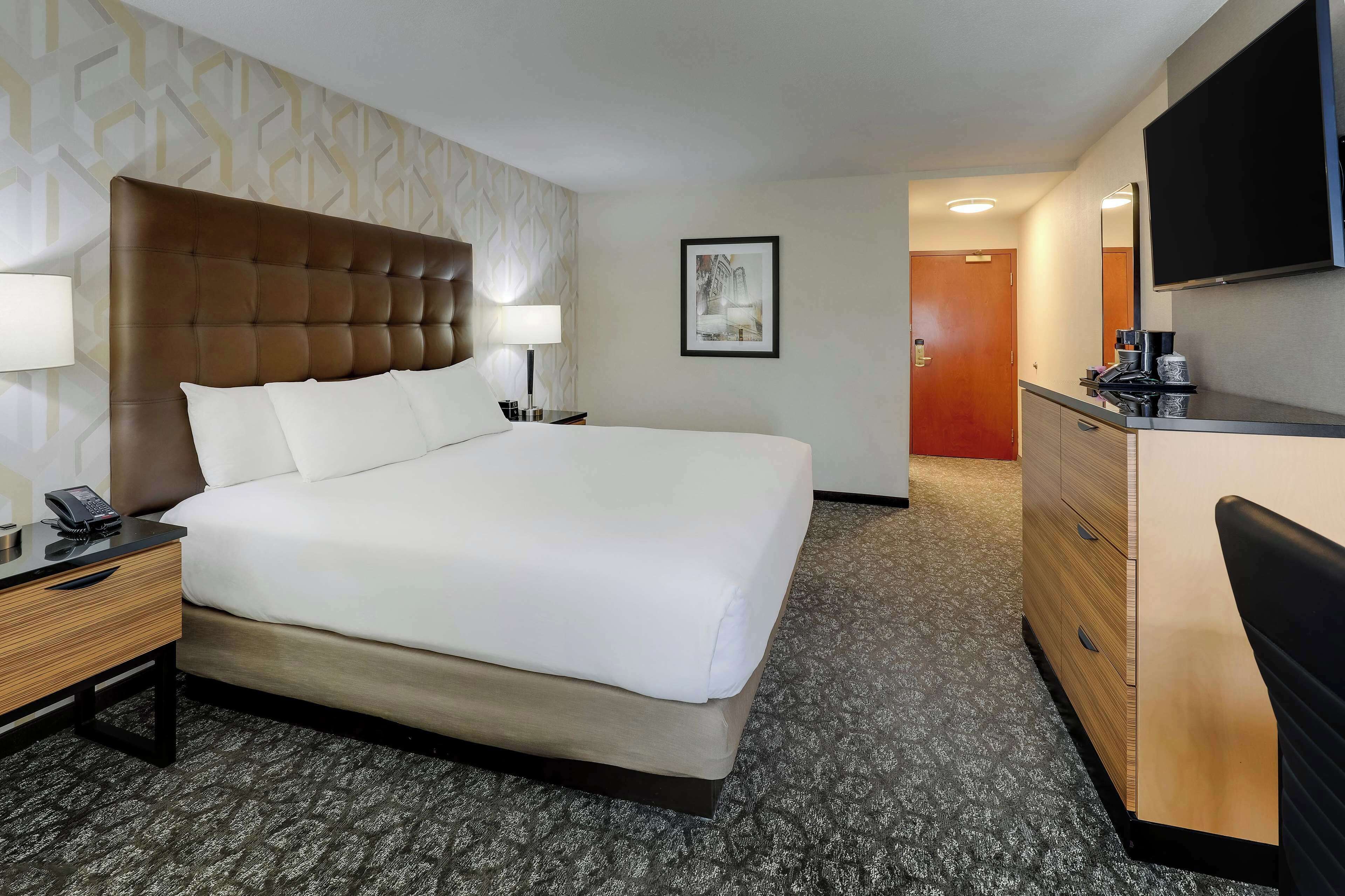 A hotel room with a large bed, bedside tables, a dresser, a flat-screen TV, and a framed picture on the wall.