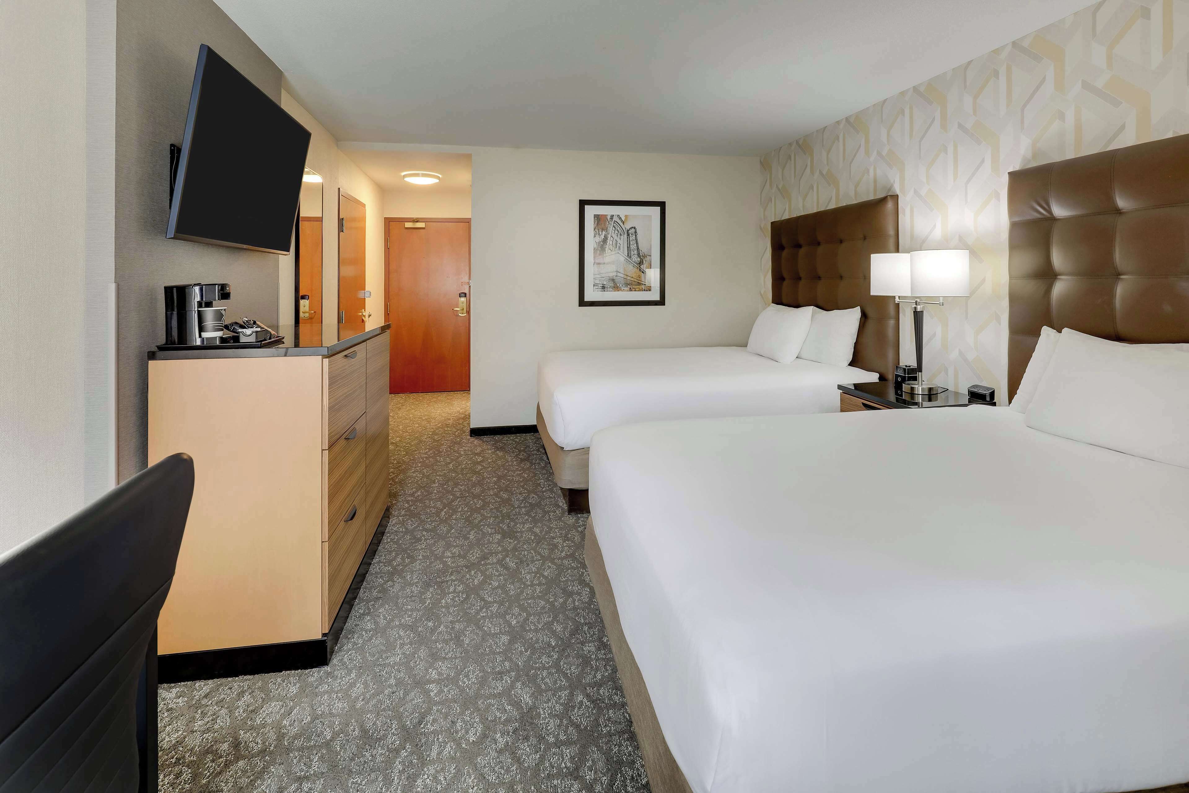 A hotel room with two beds, a desk with a flat-screen TV, a coffee maker, and a framed picture on the wall.