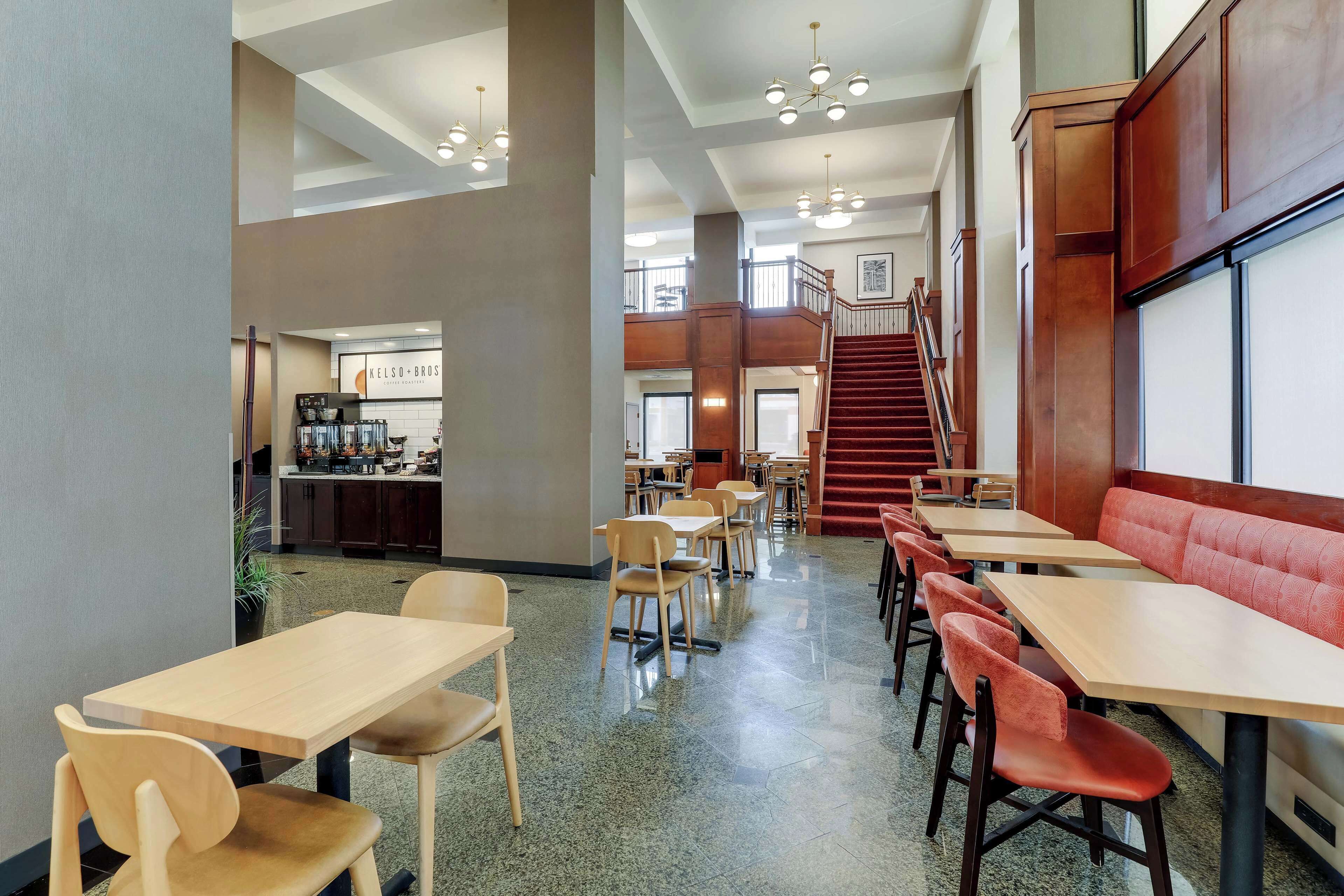A spacious indoor area with multiple seating arrangements, including tables and chairs, and a staircase leading to an upper level.