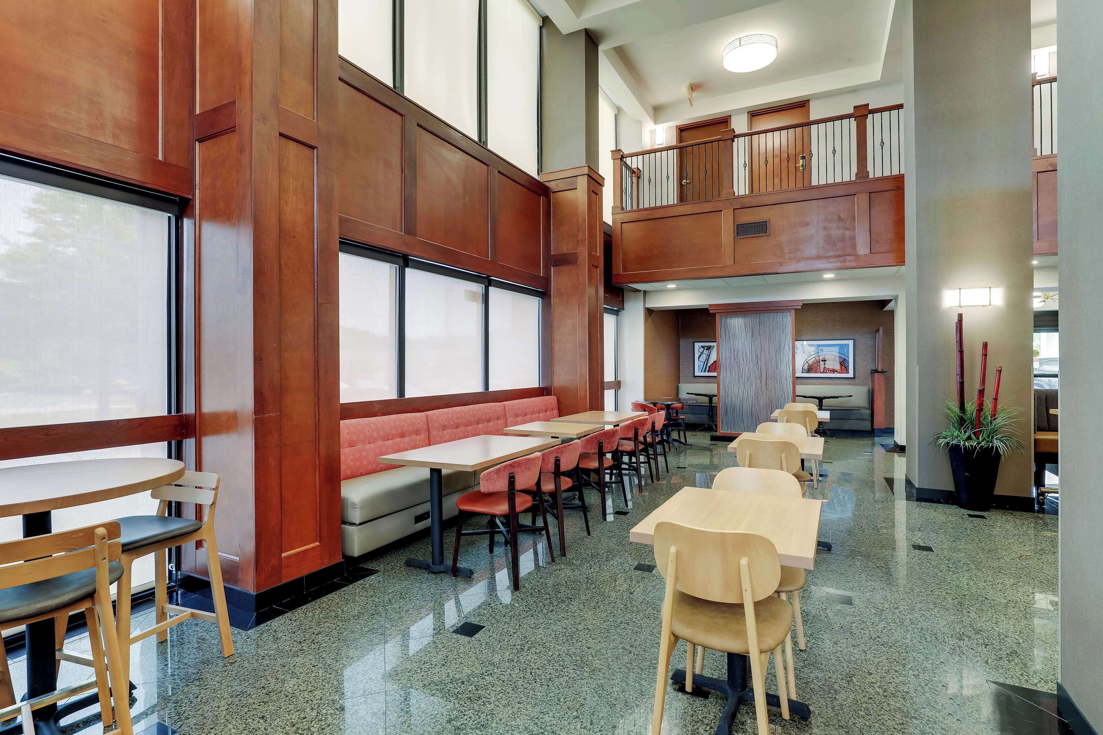 A spacious indoor area with long tables and chairs, a red bench, and a staircase leading to an upper level.