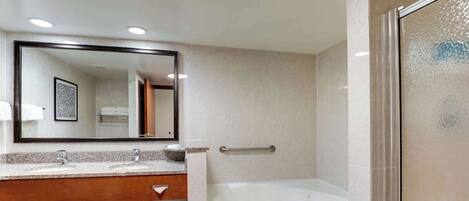 A modern bathroom with a large mirror, two sinks, a bathtub, and a shower area.